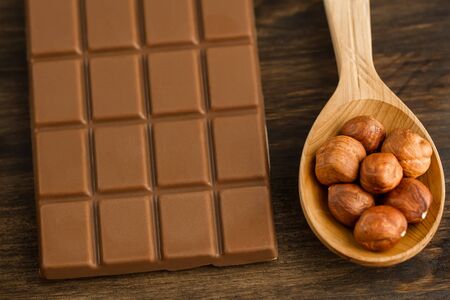 chocolate bar and peeled hazelnuts in spoon on wooden background