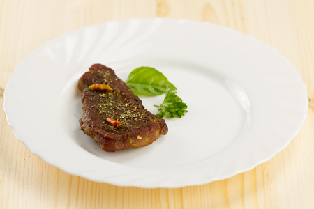 roast pork on white plate on wooden background with vegetables and herbsの写真素材
