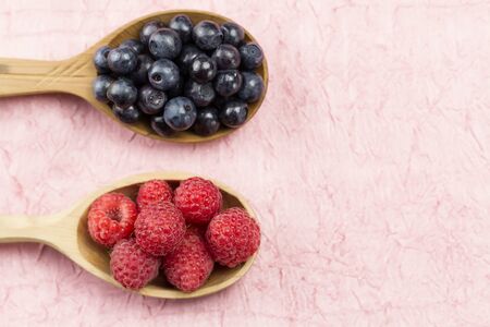 Blueberries and raspberries in a wooden spoon on a pink napkin. Healthy vegetarian food, diet.の写真素材