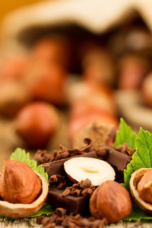 hazelnut with chocolate bars and green leaves on old wooden backgroundの写真素材