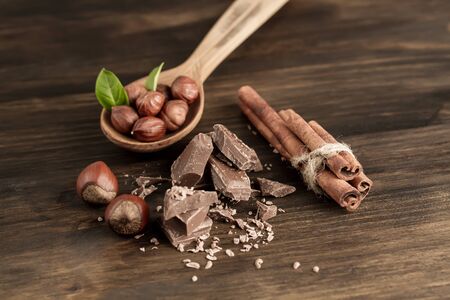 Broken chocolate bar, hazelnut and cinnamon on wooden background, close-upの写真素材