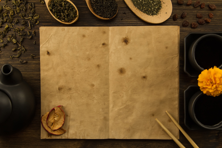 Black teapot, two cups, a collection of tea, dried apples, old blank open book on wooden background. Menu, recipe, mock upの写真素材