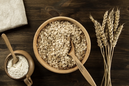 oatmeal flakes in a wooden bowl with a spoon, ears of wheat, pot of flour on the table. homemade, menu, recipe, mock upの写真素材