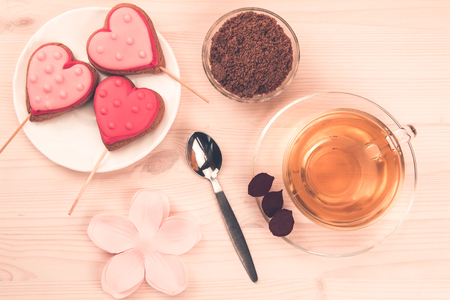 delicious fresh cookies in the shape of a heart on a white plate on wooden background. Cup of green tea. Breakfastの写真素材