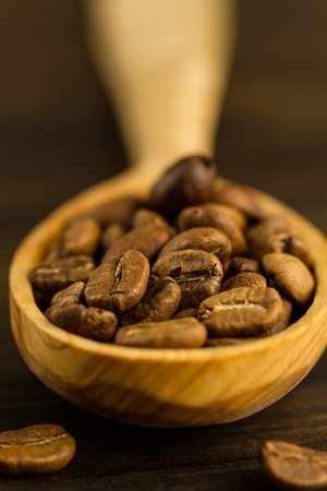 roasted coffee beans in spoon on wooden background, close upの写真素材