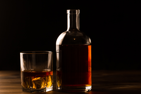 glass of whiskey with ice and a bottle on a wooden table. Cognac, brandy.の写真素材