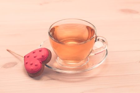 delicious fresh cookies in the shape of a heart on a white plate on wooden background. A Cup of green tea.Breakfastの写真素材