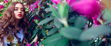 Beautiful young girl with lush hair in paradise garden. A luxurious dress, make-up. Pink flowers, large green leaves, Banner, advertising, fashion, beauty, spa. Bright, rich picture.の写真素材