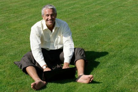 Barefoot businessman sitting on grass with laptop computerの写真素材