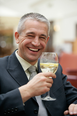 Handsome mature gray-haired businessman drinking wine glass of mineral water sitting in restaurantの写真素材