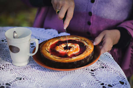 Woman hands cutting berry pie. The cake is on the table with a white lace tablecloth standing next to a cup of tea. Business diagram concept.の写真素材