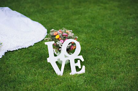 Love - wooden inscription for wedding on green grass next to flowers . Wedding decor. Flowerの写真素材