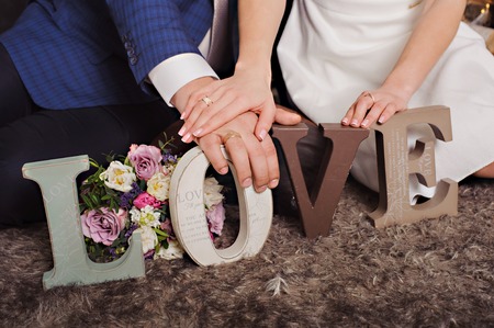 Vintage wooden inscription Love and hands of just married couple. Hands with rings, flowers, ...