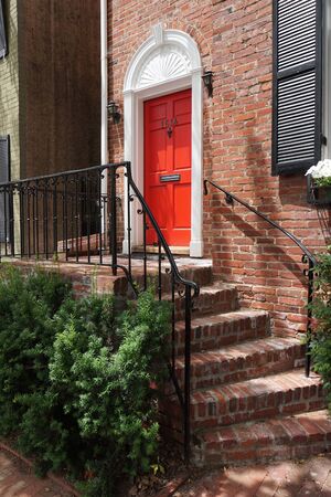 Facade of houses, stairs, windows with black shutters, red door, green bushes, verticalの写真素材