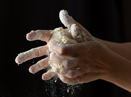 hands knead dough on a black background