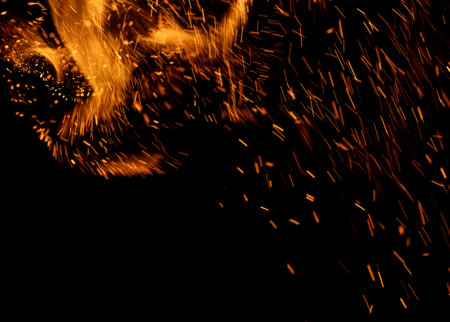 A black background with orange sparks flying in the air. The sparks are coming from a fire, and the image has a warm, fiery, and energetic moodの写真素材