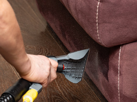 A person is cleaning a couch with a vacuum. The couch is brown and the person is using a vacuum cleaner to clean itの写真素材