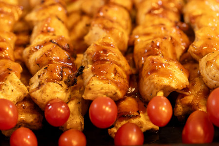 A plate of chicken skewers with a tomato on the side. The skewers are browned and glazed, and the tomato is ripe and juicy. The plate is set on a table, ready to be servedの写真素材
