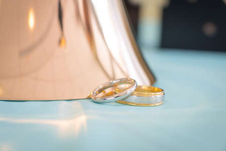 Wedding rings displayed on a light blue background with a copper hand bellの写真素材