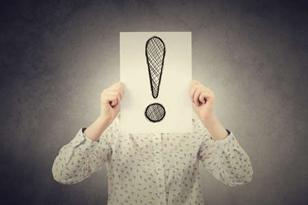 Young student,businesswoman covering his face using a paper with a exclamation mark.Finding the righ solution concept.Caution Expresionの写真素材