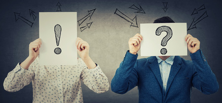 Businessman and businesswoman covering their faces using white paper sheets with drawn interrogation...