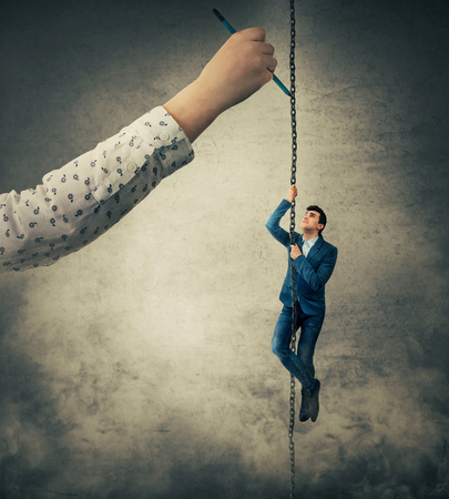 Businesswoman hand drawing a chain with a scared businessman as a marionette suspending, trying to climb up. Business manipulation, control, leadership and risk concept.の写真素材