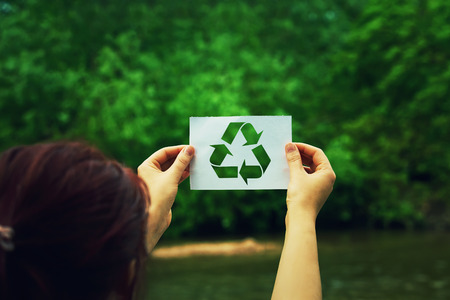 Woman holding a paper sheet with recycle symbol over green forest nature background. Ecology and greening concept.の写真素材