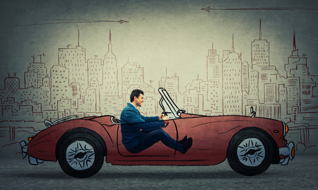 Profile portrait of a young smiling businessman driving a drawn race car in an imaginary city isolated on grey wall background.の写真素材