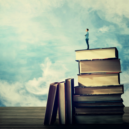 Young student stand on the top of a huge pile of books looking far at horizon. Idea and knowlegde concept.の写真素材