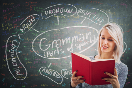 Teacher holding a red book over blackboard background written with chalk english grammar parts of speech. Opportunity for students to learn the system and structure of a language.の写真素材