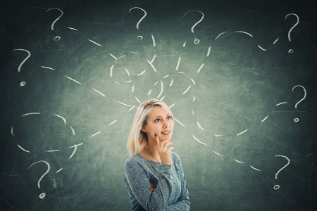 Puzzled young woman in front of a blackboard try to solve different tasks, having a lot of questions. Inspiration concept and self development.の写真素材