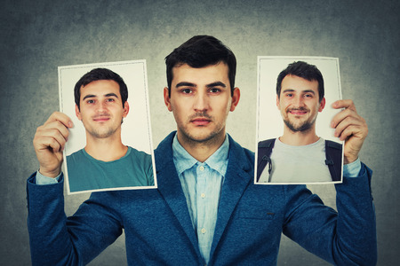 Young man holding two portrait photo sheets with different character. Change your personality, fake mask to hide the real expression of yourself.の写真素材