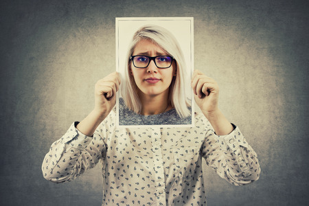 Young businesswoman undercovered by another person using a photo portrait sheet, like a mask to hide her real personality and emotion. Create fake identity concept.の写真素材