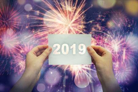 Woman hands rised up to the sky holding a white paper sheet with 2019 text in the middle. New year...