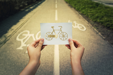 Close up of woman hands holding a white paper sheet with bicycle icon over bike lane background.の写真素材