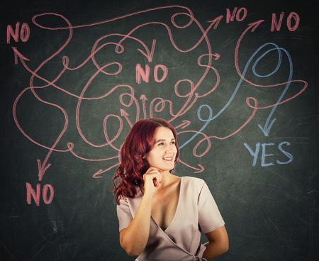 Smiling smart woman in front of a blackboard finding correct answer to her questions as curves arrows from head leading to yes or no response. Difficult choice concept.の写真素材