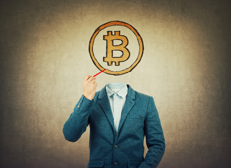 Surreal image as a businessman with invisible face holding a pencil in his hand draw bitcoin icon instead of head. Modern technology, virtual cryptocurrency concept.の写真素材