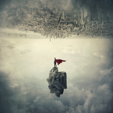 Confident superhero with red cape standing on a levitating stone underneath the cityscape. Imaginary world upside down, mystical scene flying super power.の写真素材