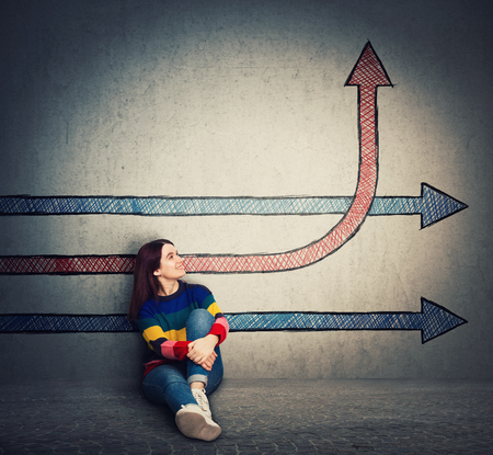 Casual young woman sitting on the floor looking at arrows one changing direction, benting go up, as a progress raising graph. Life change and growth symbol, different thinking, alternative idea.の写真素材