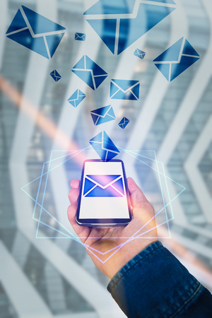 Man hand blue jeans jacket holding a mobile phone sending messages as coming out of screen interface. Envelope message hologram icon. Modern technology concept virtual reality social life.の写真素材