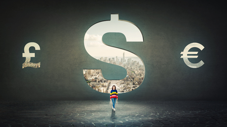 Confident woman standing alone in front of a dollar sign hole as a door shaped in a concrete wall with a view to the city. Financial success concept.の写真素材