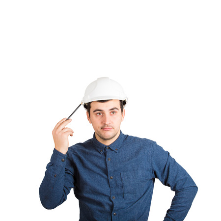 Pensive young man engineer wearing protective helmet thinking pointing pencil to head isolated over white background with copy space.の写真素材