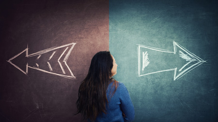Puzzled woman rear view and split blackboard with arrows going in two different ways red and blue side. Correct choice between left and right, failure or success. Difficult decision and doubt concept.の写真素材
