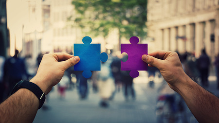 Two hands holding different colored puzzle pieces, unite jigsaw over a crowded street background....