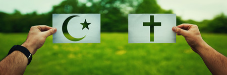 Religion conflicts as global issue concept. Two hands holding different faith symbols, Islam vs Christianity belief over green field nature. Relations between different people doctrines and church.の写真素材