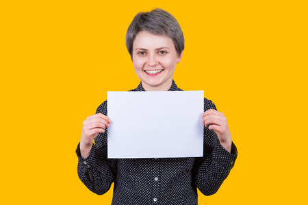 Pretty young woman hipster holding a blank paper sheet for advertising, looking cheerful to camera...