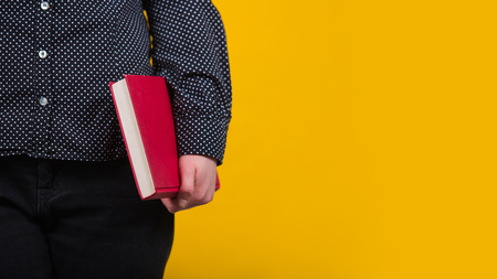 Close up of young woman holding a red book close to body. Education concept, student girl choose a textbook for reading isolated over yellow background with copy space.の写真素材