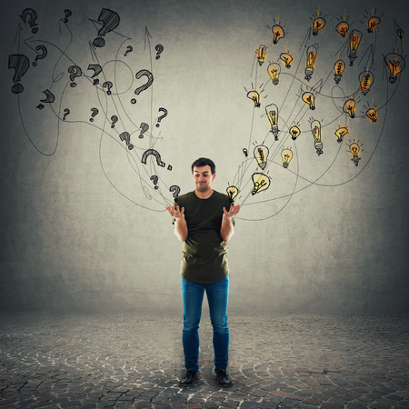 Perplexed young man has different questions and ideas as holding interrogation marks in one palm and light bulbs in another. Unsure thoughtful guy making the right choice.の写真素材