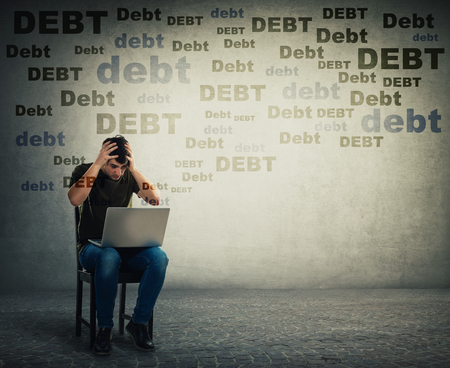 Upset and stressed young man using laptop seated on a chair, holding hands to head, has emotional shock about huge debt amount. Disappointed freelancer guy overspending, has no money in bank account.の写真素材