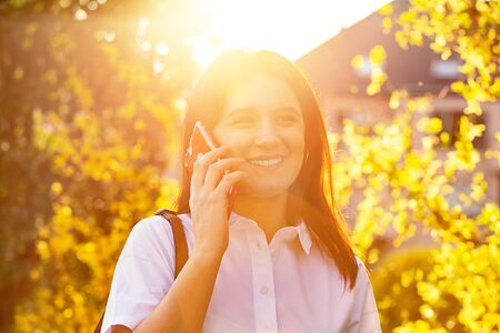 Smiling Young student with mobile phone outdoor in the sunset. Happy Young Business Woman receiving good news via cell phone. Male entrepreneur in formal clothes received news about work.の写真素材